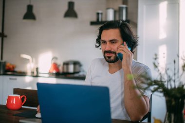 Evdeki işyerinde. Bir adam evde dizüstü bilgisayarda çalışıyor, gün boyunca oturma odasında bir masada oturuyor, telefonla konuşuyor. Evden çalış..