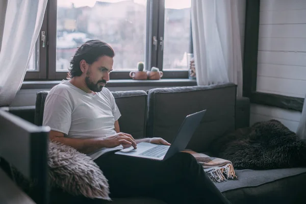 在家工作 一个男人在家里的笔记本电脑上工作 白天坐在客厅的沙发上 打电话 在家工作 — 图库照片