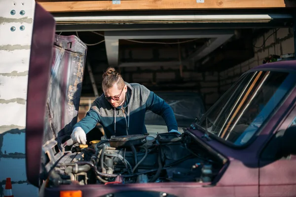 A man repairs a car, opens the hood. A young guy looks under the hood of a car, self repair in a private garage