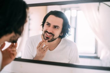 Yakışıklı bir adam aynaya bakar. Erkeklerin kişisel bakımı. Genç bir adam yatak odasındaki aynada kendini muayene ediyor..