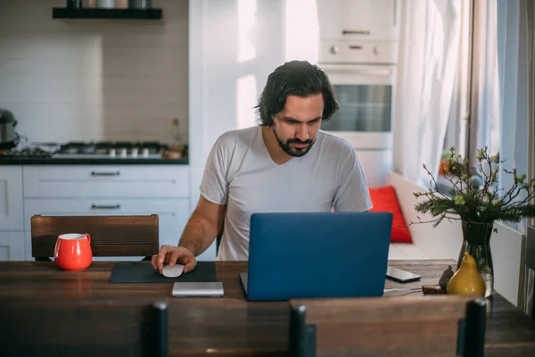 Workplace at home. A man works at a laptop at home, sits at a table in the living room during the day. Work from home.