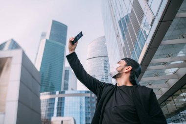 Issız bir şehirde elinde telefon olan bir adam. Genç bir adam, boş bir metropoldeki akıllı telefondan gökdelenleri alıyor.