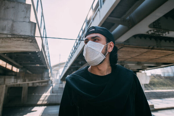 A man in a medical mask on an industrial background. Lonely young guy in a mask on a background of empty roads and overpasses in a metropolis