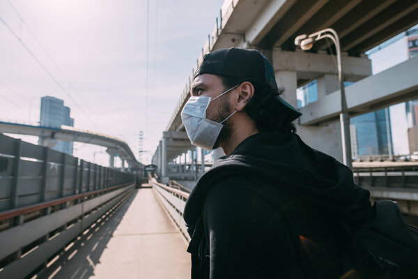 A man in a medical mask on an industrial background. Lonely young guy in a mask on a background of empty roads and overpasses in a metropolis