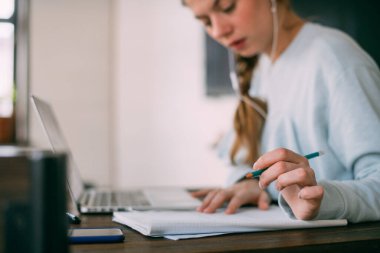 Dizüstü bilgisayarı olan bir kadın not alır, internetten yabancı bir dil öğrenir, çevrimiçi eğitim kursu, internette eğitim, videodaki bir müşteriye danışmanlık yapar. Ön planda bir kalem ile el.