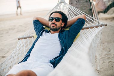 Bir adam sükunetten hoşlanır, okyanusun arka planında bir hamakta yatar ve günbatımını seyreder. Yakışıklı adam tropik bir adanın sahilinde gün batımıyla karşılaşır..