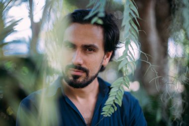 Yeşil yapraklı bir adamın kavramsal portresi. Güzel esmer adam, tropik çalıların arasında poz veren bir model. Yakın plan.