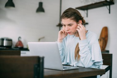 Bir kadın oturma odasında dizüstü bilgisayarla oturuyor, ekrana bakıyor, notlar alıyor, internetten yabancı bir dil öğreniyor, online eğitim kursları okuyor, internetten eğitim alıyor, bir müşteriye danışmanlık yapıyor.