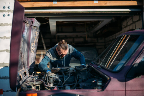 A man repairs a car, opens the hood. A young guy looks under the hood of a car, self repair in a private garage