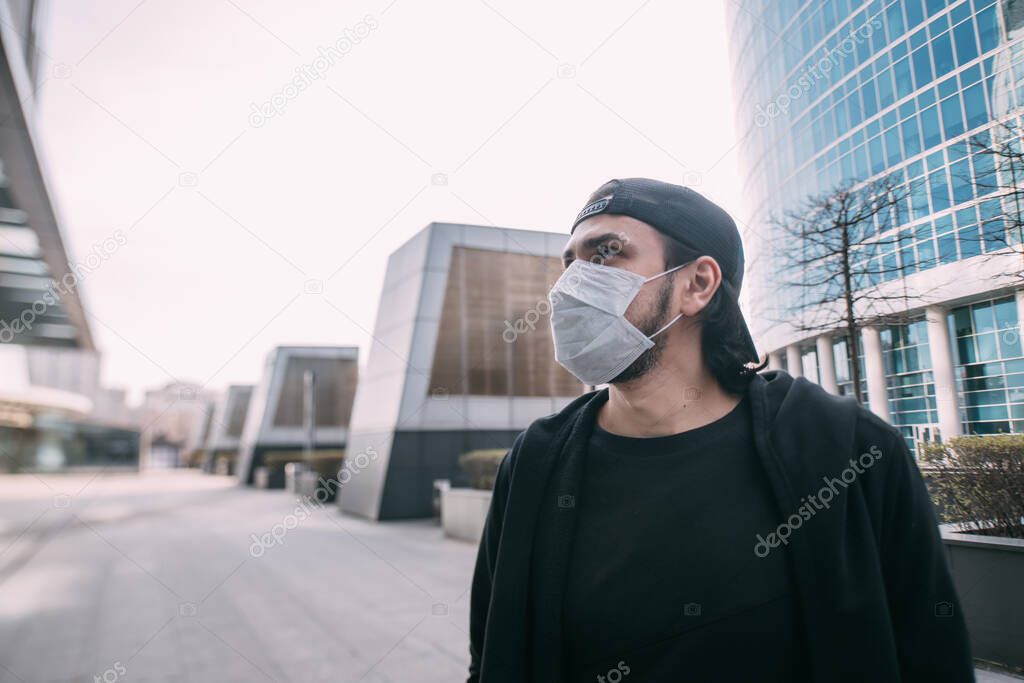 A man in a medical mask on an industrial background of skyscrapers. Lonely young guy in a mask in an empty metropolis. Man and huge city in quarantine.