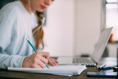 Dizüstü bilgisayarı olan bir kadın not alır, internetten yabancı bir dil öğrenir, çevrimiçi eğitim kursu, internette eğitim, videodaki bir müşteriye danışmanlık yapar. Ön planda bir kalem ile el.