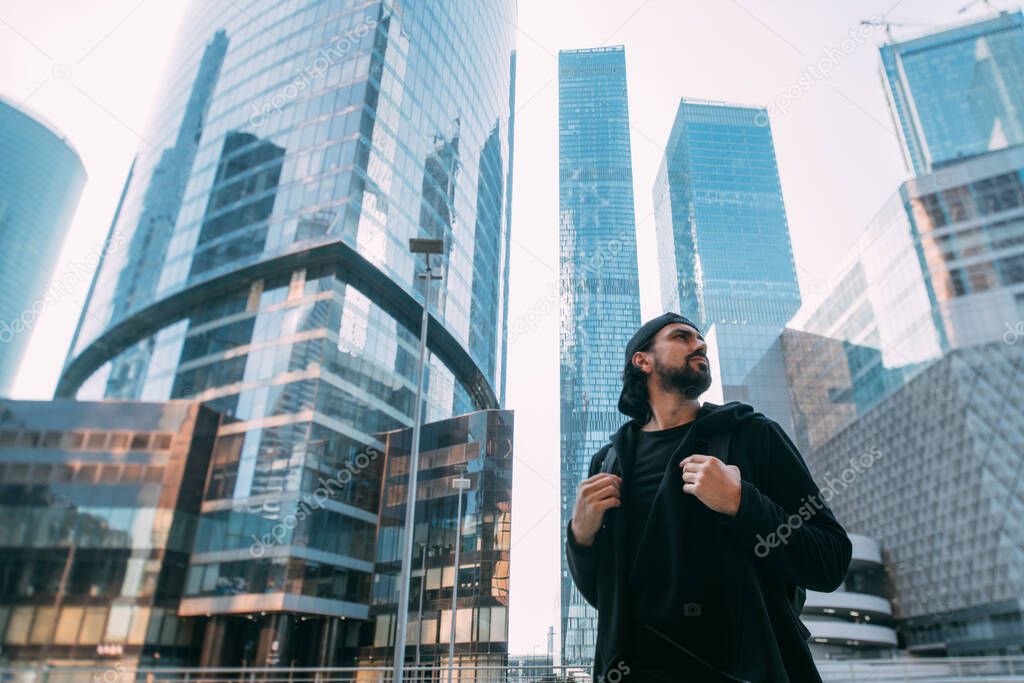 A man on an industrial background of glass skyscrapers. A lonely young guy in a metropolis. Man and a huge city.