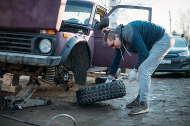 Bir adam araba tamir eder, tekerlek takar, mevsimlik lastik değiştirir. Genç bir adam tek başına araba tamir ediyor, özel bir garaja yeni tekerlekler takıyor.