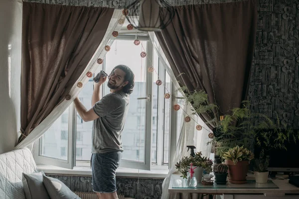 A man washes windows at home. Young handsome guy doing spring cleaning in a cozy apartment.