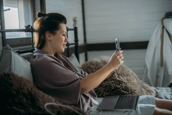 Mujer Trabaja Con Ordenador Portátil Teléfono Cama Dormitorio Una Joven —  Fotos de Stock