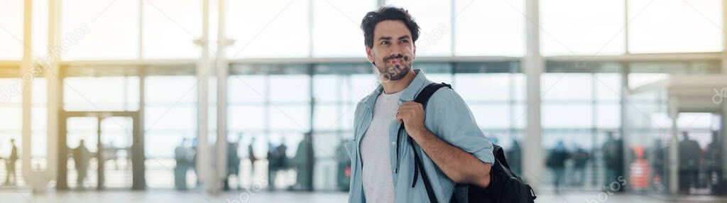 The guy with the backpack at the airport. Young handsome man waiting for boarding, walks through airport terminal