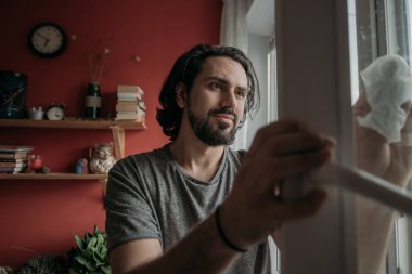 Evdeki pencereleri temizleyen bir adam. Genç yakışıklı adam sıcak bir dairede bahar temizliği yapıyor..