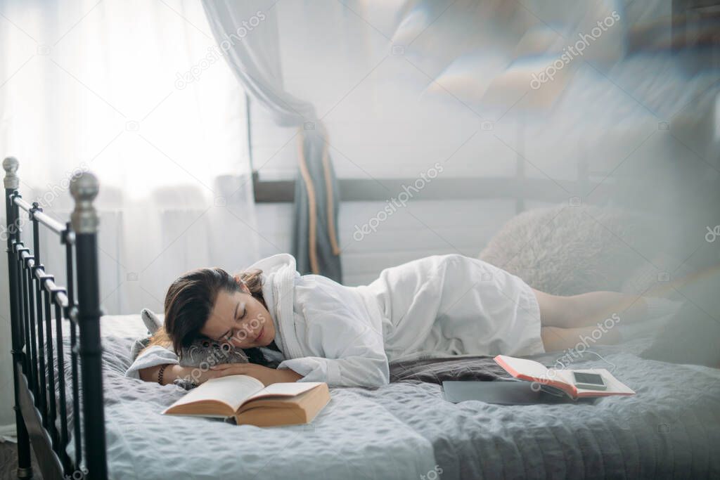 A woman in a bathrobe sleeps on a bed with a book. Young girl resting, dozing in the bedroom on a large cozy bed in the afternoon