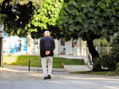 Elleri arkada yürüyen yaşlı bir adam.