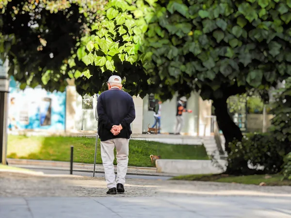 Elleri arkada yürüyen yaşlı bir adam.