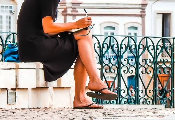 Woman in black dress writing something sitting on a curb