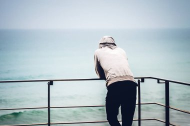 Arkadan, korkulukların desteklediği denize bakan adam görüldü.