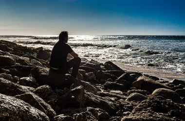 Siyah adam deniz kıyısında kayaların üzerinde duruyor.