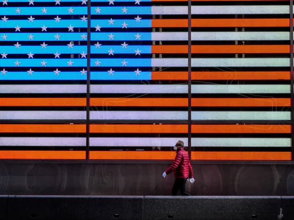 Nova York, Estados Unidos, EUA 24 de março de 2020: velho homem asiático com máscara e globos andando frente aos estados unidos da bandeira da américa em tempos quadrados durante a pandemia de coronavírus — Fotografia de Stock