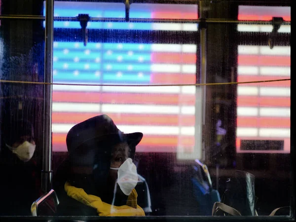 New York, États-Unis, États-Unis 24 mars 2020 : femme afro-américaine fatiguée, portant un masque, assise dans un bus pendant une pandémie de coronavirus devant un drapeau américain, temps carrés — Photo