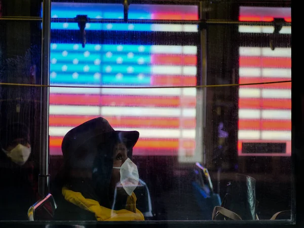 Nova York, Estados Unidos, EUA 24 de março de 2020: mulher afro-americana esperançosa vestindo uma máscara, sentada em um ônibus durante a pandemia de surto de coronavírus na frente da bandeira americana, vezes quadrada — Fotografia de Stock
