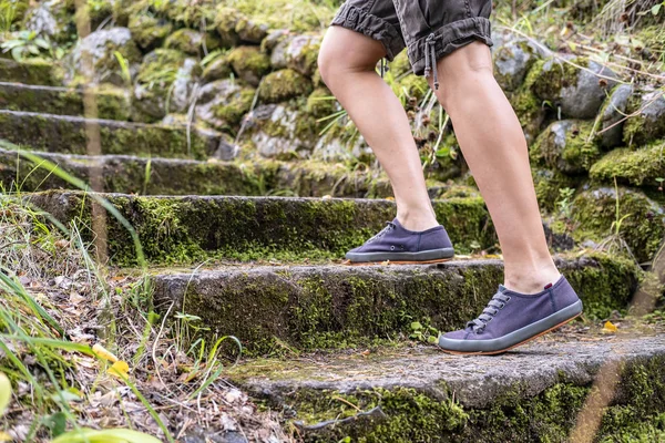 Gambe femminili in scarpe da ginnastica, risalendo i vecchi gradini in pietra, sullo sfondo di un muro di ciottoli. Concetto di stile di vita attivo . — Foto Stock