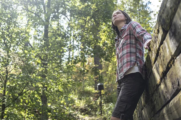 Jolie femme admire la belle forêt, debout près du vieux mur de rondins dans le parc, par un été, journée ensoleillée . — Photo