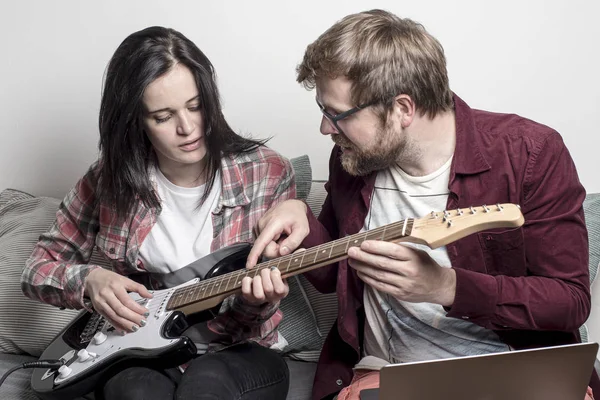 Man teaches a woman to play a six-string electric guitar.