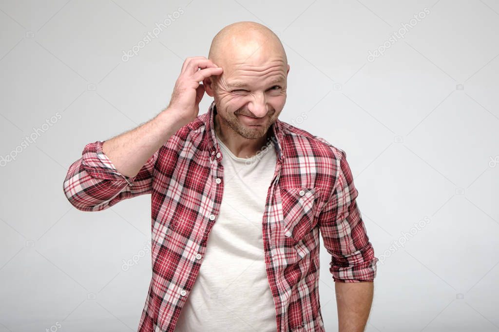 Bald man with stubble on face, looks into the camera with repentance, smiles guiltily and narrows one eye.