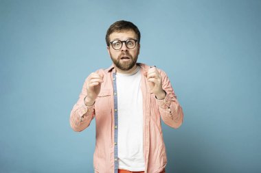 Gözlüklü sakallı adam, beklenmedik bir sürpriz karşısında şaşkın ve heyecanlı. Mavi bir arkaplanda izole edilmiş.