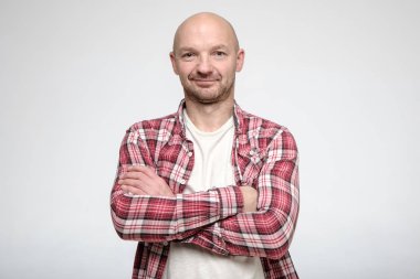 Kendinden emin, kel, traşsız adam kollarını kavuşturup kameraya bakıyor..