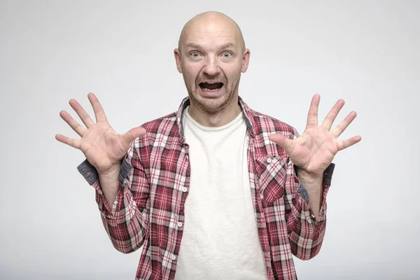 Kale man met gekke ogen en een open mond, hief zijn handen op en probeert iemand bang te maken. — Stockfoto