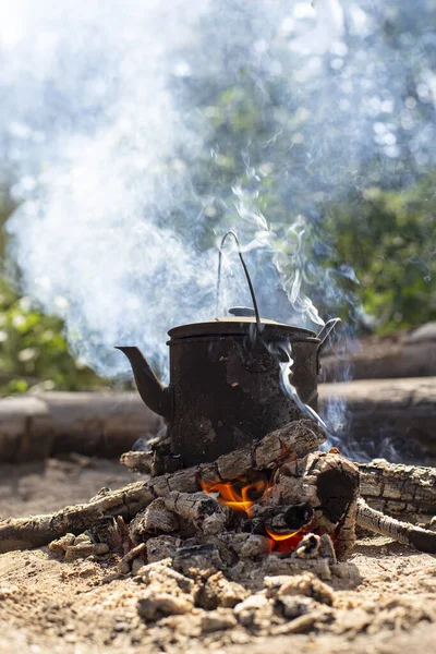 Βραστό, καπνιστό βραστήρα με ζεστό ρόφημα στέκεται σε μια φωτιά στον καπνό, σε ένα δάσος. — Φωτογραφία Αρχείου