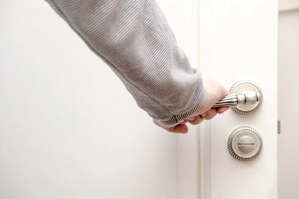 Mano umana aggrappata ad una bella maniglia in metallo intagliato in una porta di legno aperta, dipinta di colore bianco . — Foto Stock