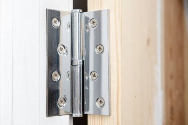 Ahşap kapıdaki parlak metal menteşe bir kısmı beyaza boyanmış, diğer kısmı ise beyaza boyanmamış. Ev onarımı.