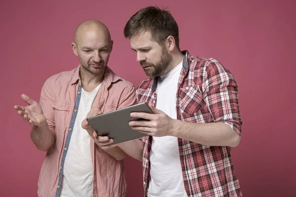 Two puzzled men, with a serious expression on their faces, are discussing some problem, looking at the tablet.