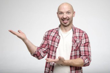 Yüzünde aptal bir ifade olan kel bir adam elleriyle bir jest yapıyor ve dili dışarı sarkık kameraya bakıyor..