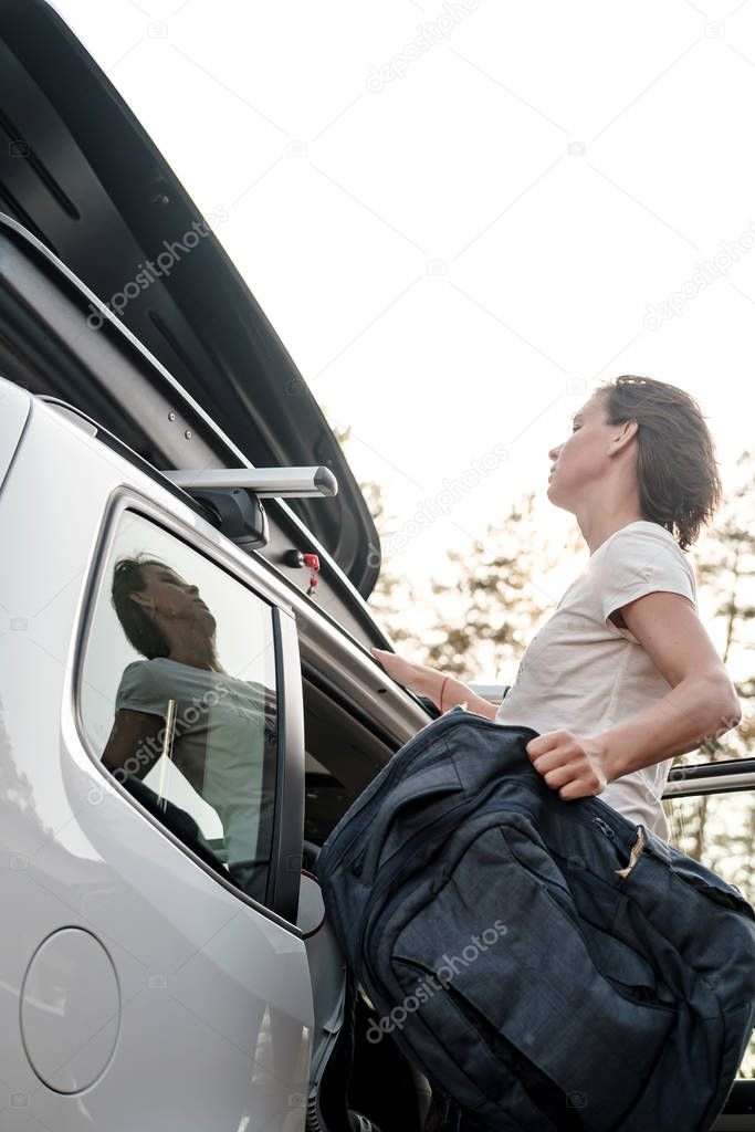 Focused woman puts things in the roof rack of a car or in a cargo box. Preparing for a vacation.