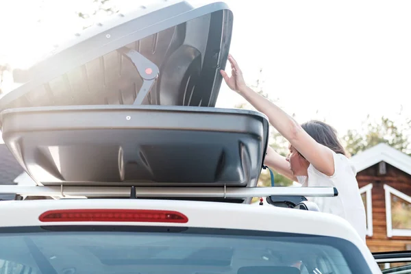 Mujer enfocada mirando dentro de un baúl abierto o caja de carga, que está en el techo de un coche. Preparación para unas vacaciones . — Foto de Stock