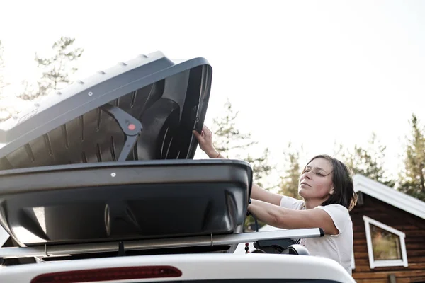 Mujer abre el maletero o caja de carga, que se encuentra en el techo del coche. Preparación para unas vacaciones . — Foto de Stock