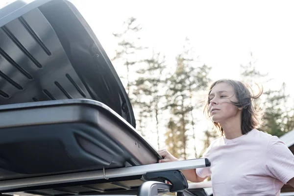 Tronco abierto o caja de carga, que se encuentra en el techo de un coche y una mujer espiando en él. Preparación para unas vacaciones . — Foto de Stock