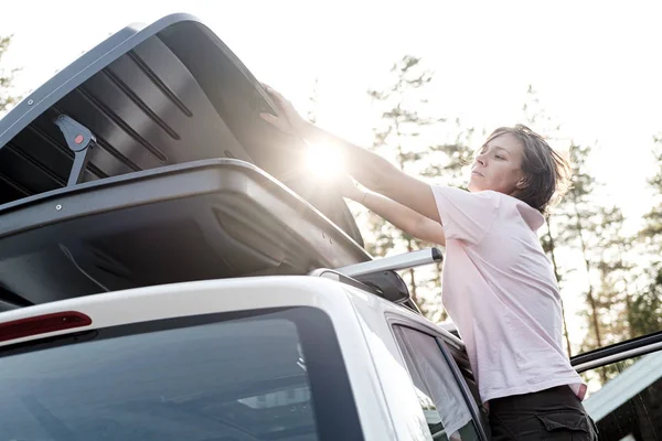 La mujer cierra un baúl lleno de cosas, que está en el techo de un coche, el día de verano. Vacaciones familiares . — Foto de Stock