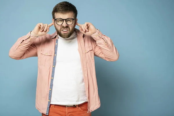 Vreemde man met een grappige grimas drukt vingers aan de oren en probeert iets te horen en kijkt met vernauwde ogen naar de camera. — Stockfoto