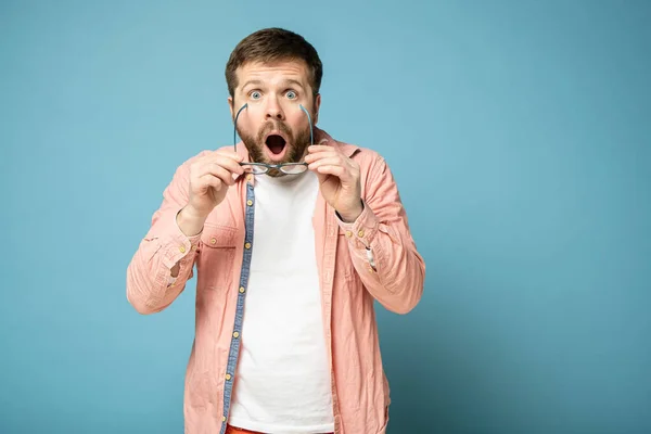 Caucasian guy in a coral shirt, surprised and shocked, he took off glasses, opened mouth and looks with big eyes into the camera. — 스톡 사진