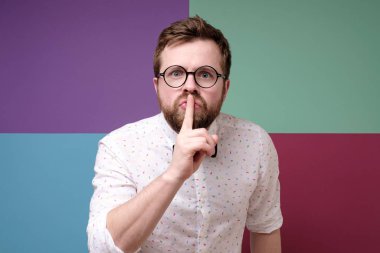 Adam işaret parmağını dudaklara koyar, sessizliği ifade eder, gürültü yapmaz, bir sır saklar ve kameraya bakar. İşaret dili.